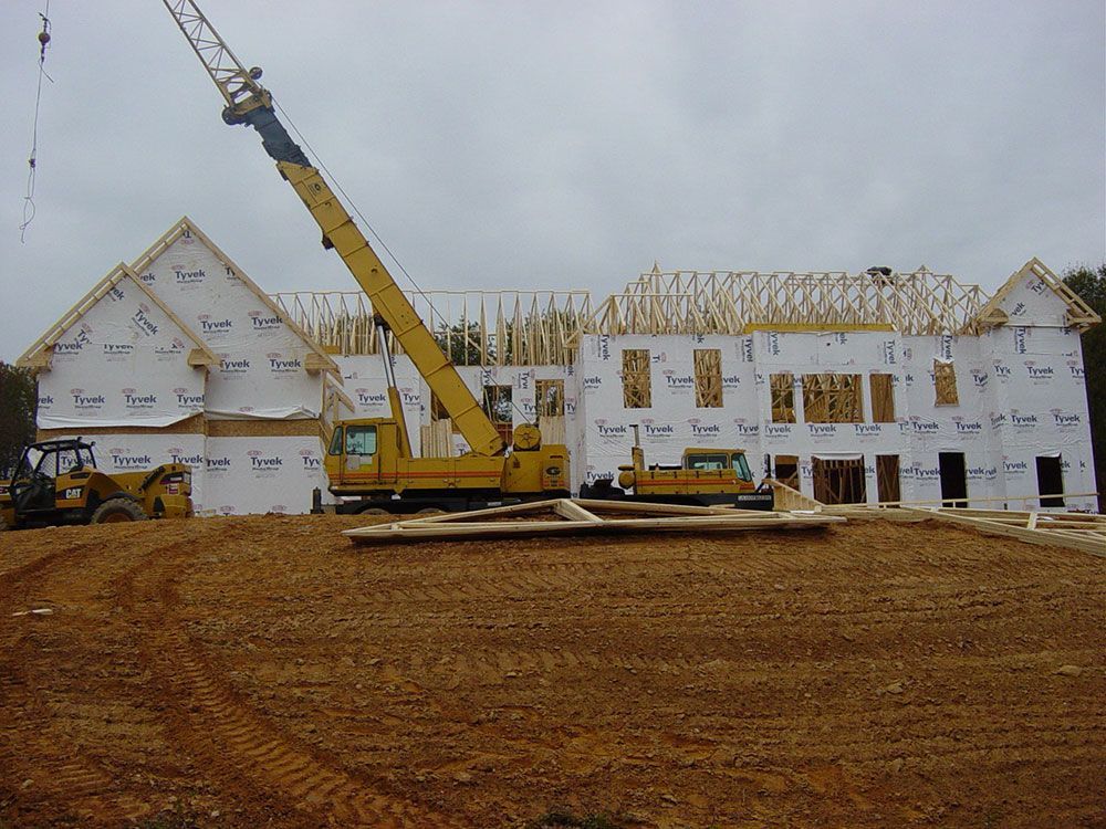 A large yellow crane is sitting in front of a house under construction