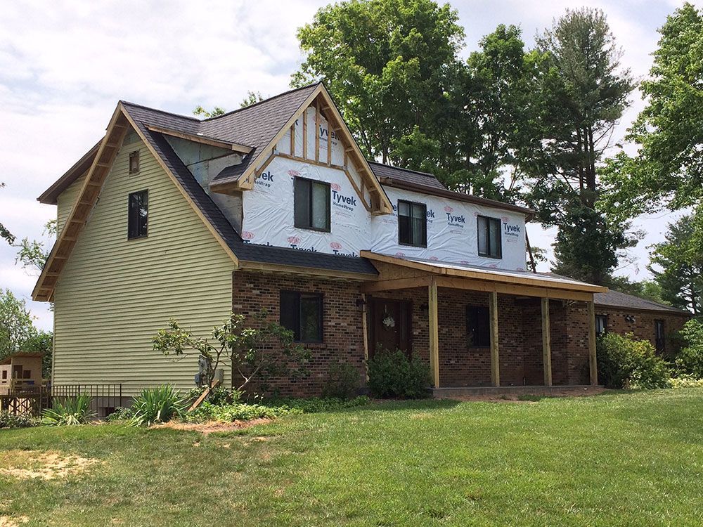A large house with a porch is sitting in the middle of a grassy field.