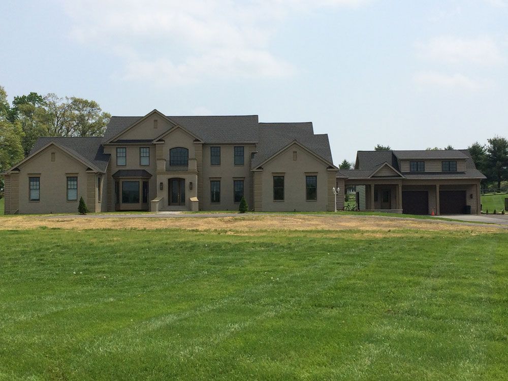 A large house sits in the middle of a lush green field