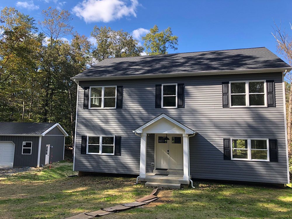 A large gray house with black shutters and a garage next to it.