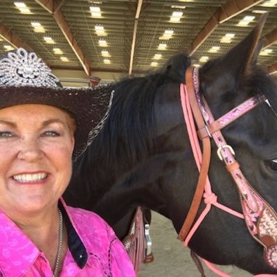 A woman in a cowboy hat is standing next to a black horse