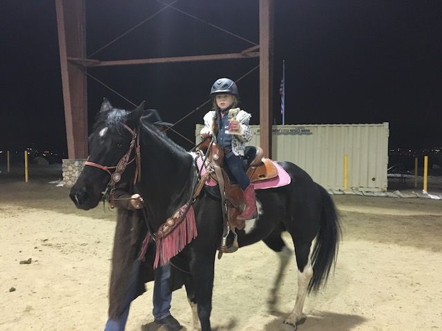 A girl is riding a black horse with a pink saddle