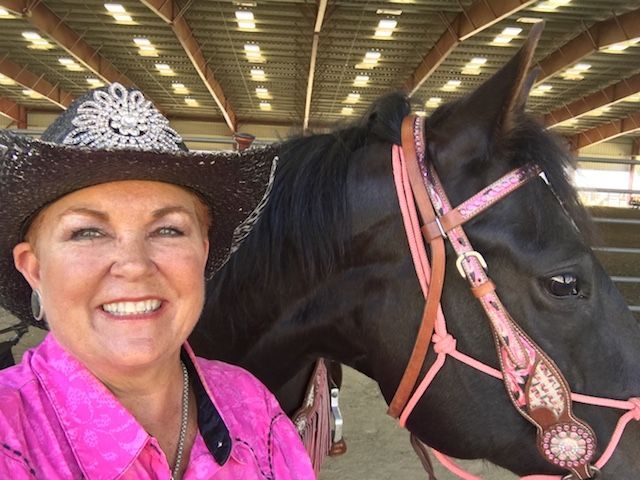 A woman wearing a cowboy hat is standing next to a black horse