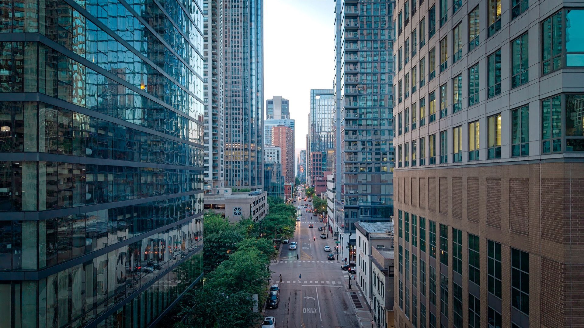Downtown city street between tall office buildings, with traffic and pedestrians in the distance.