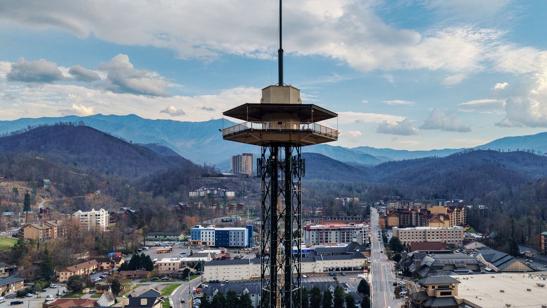 Tall observation tower above a city with mountains and cloudy sky in the background
