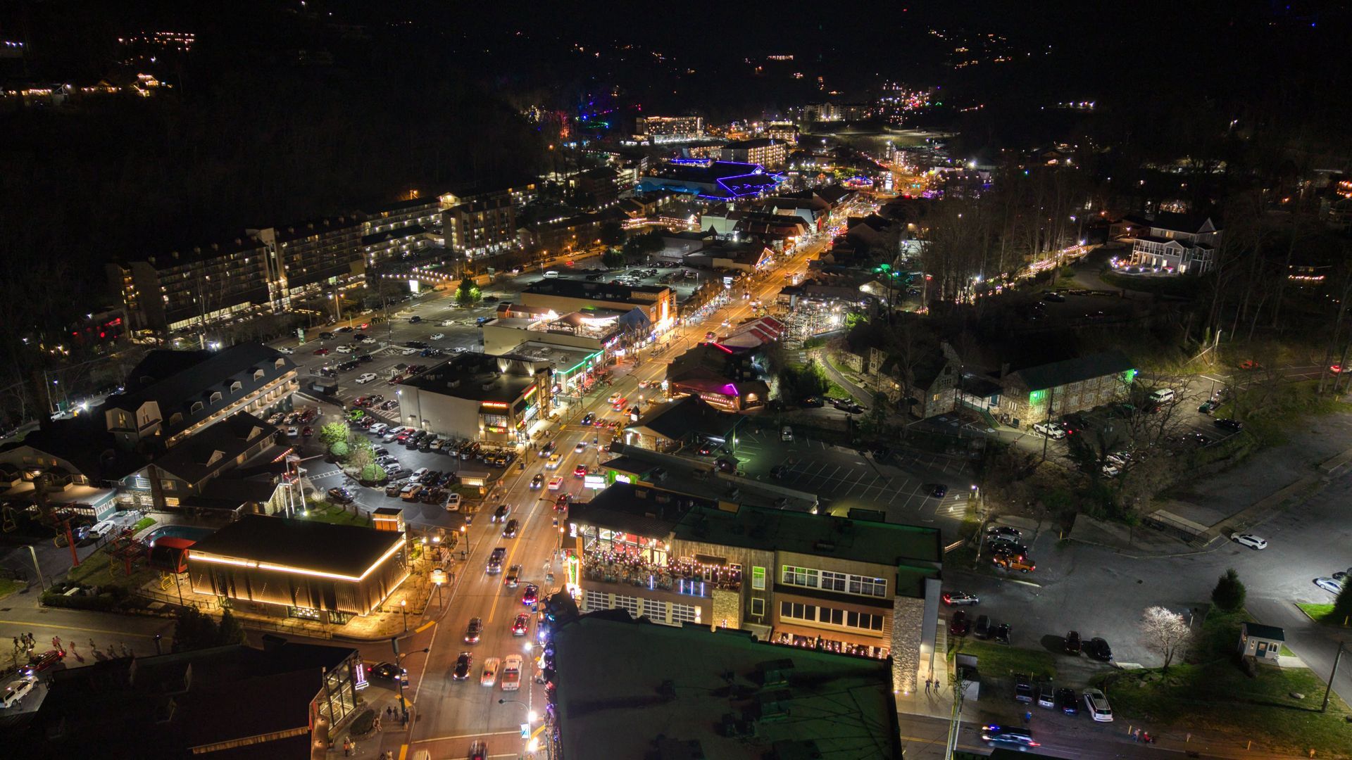 Nighttime aerial view of a busy city street lined with bright lights and moving traffic