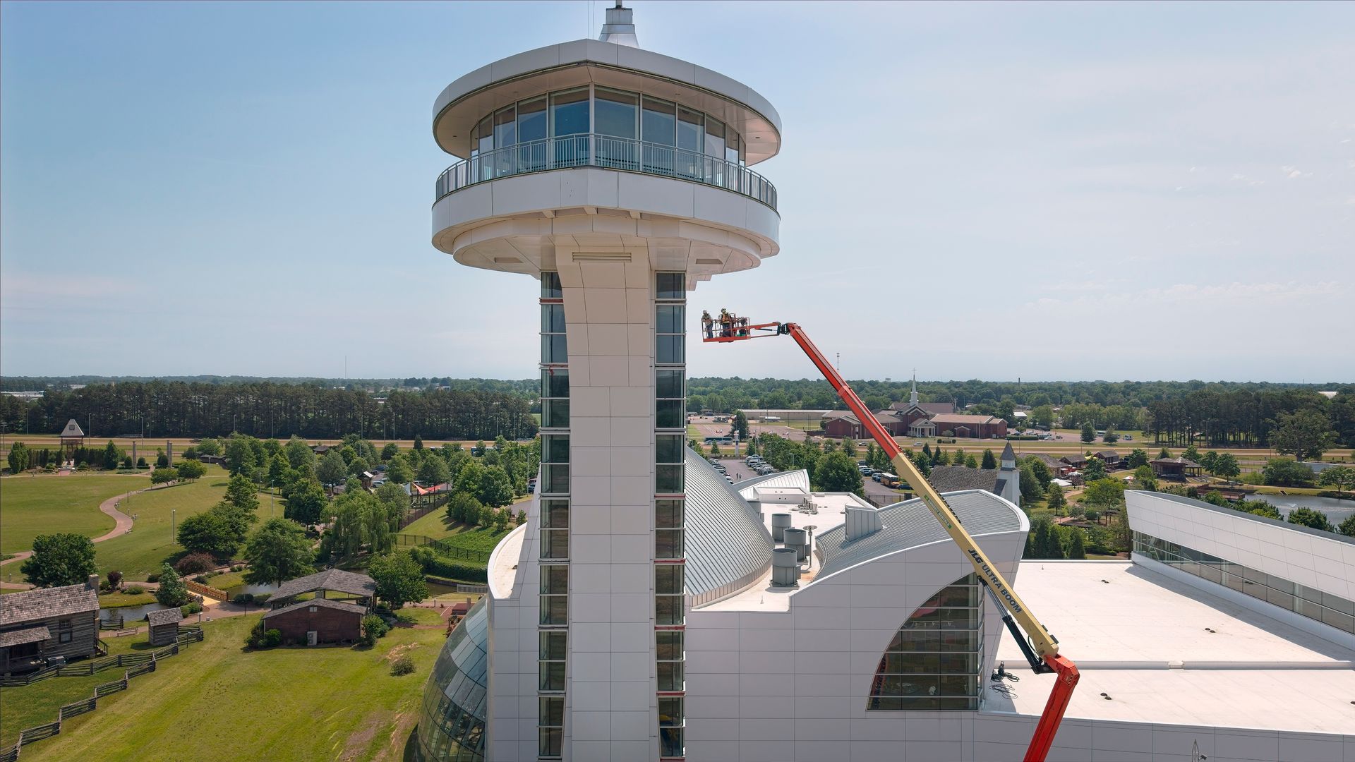 Aerial view of a tall control tower beside a white-roofed building with a crane lifting materials nearby.