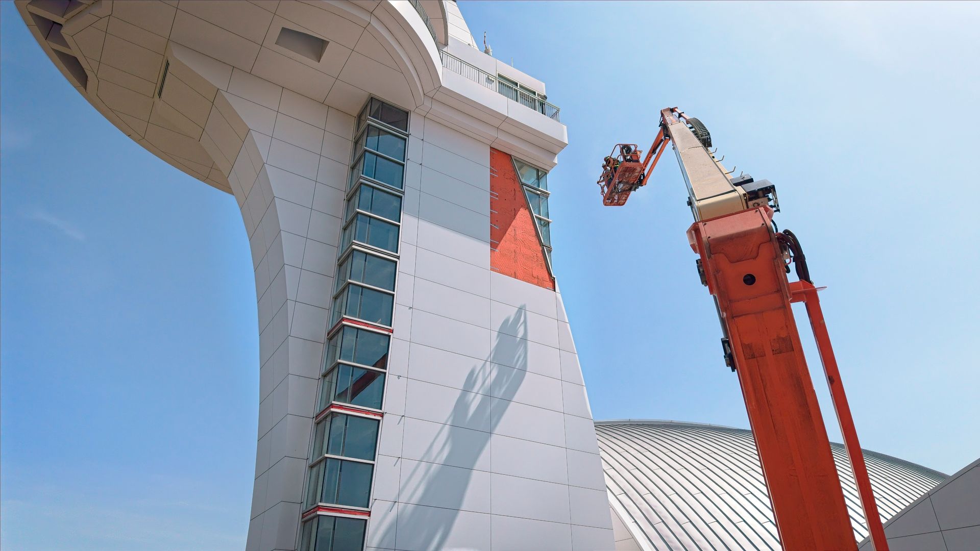 Tall white structure with red-orange lift equipment beside it under a blue sky