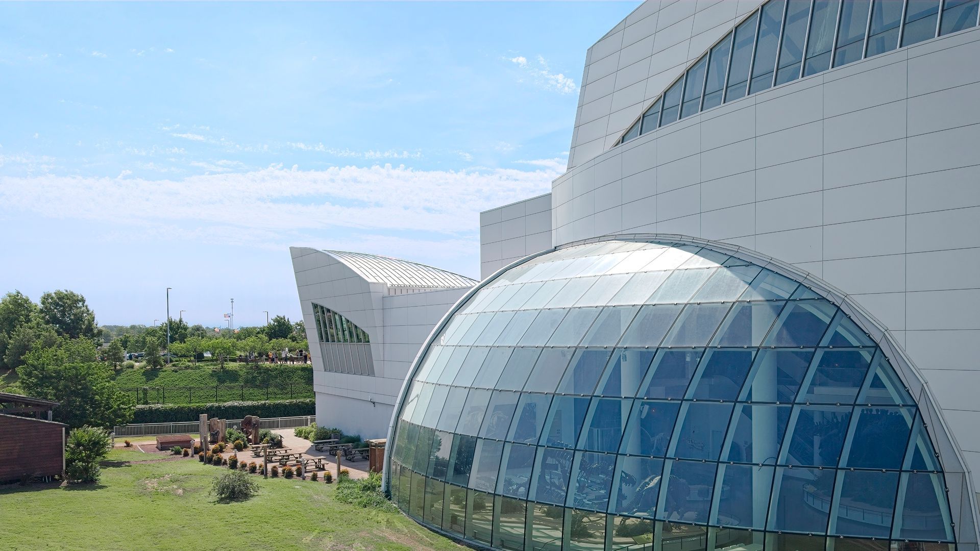 Modern building with a curved glass dome and landscaped green area under a blue sky