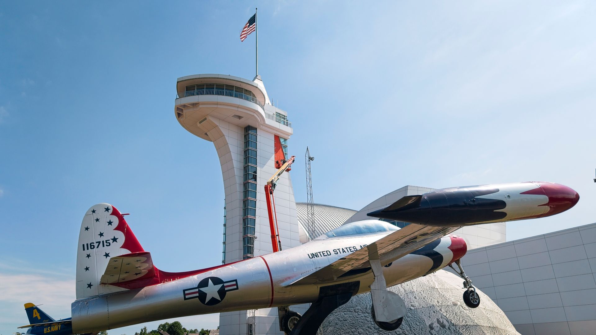 Vintage fighter plane display in front of an airport control tower under a clear blue sky