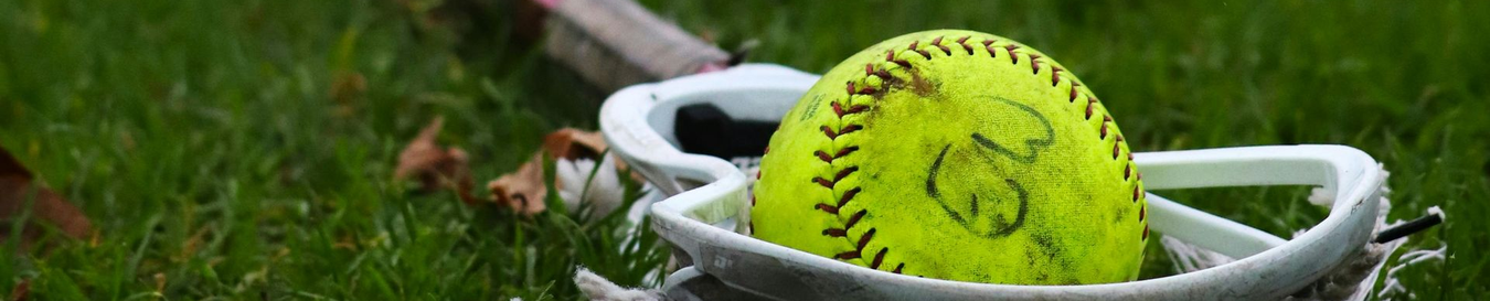 Baseball glove with ball on green grass, with blurred baseballs in the background.