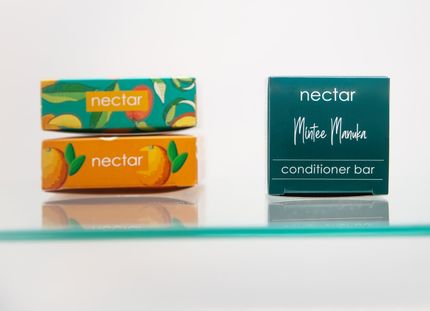 Two soap bars and a conditioner bar on a glass shelf; the bars are boxed in green and orange with peach illustrations.
