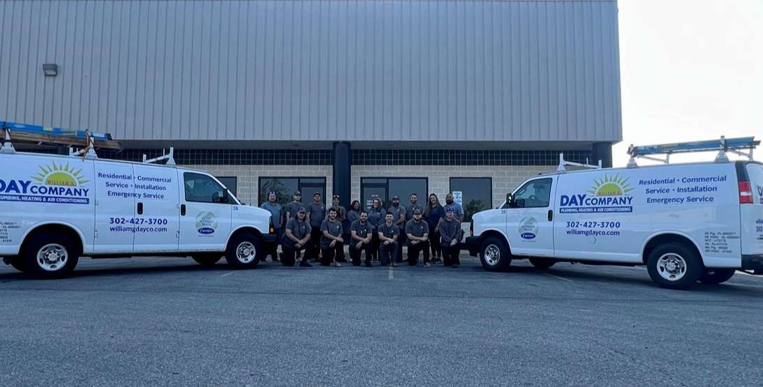 Two white service vans parked outside a warehouse with a group posing between them