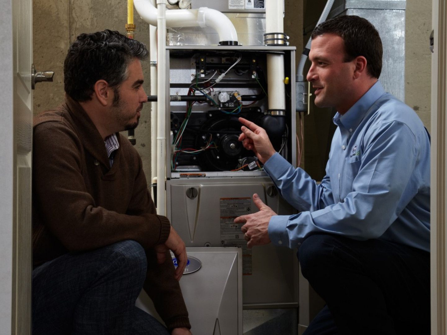 Two men talking in a mechanical room beside pipes and equipment.