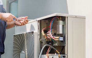 Technician repairing an outdoor air conditioner unit with exposed wiring and components