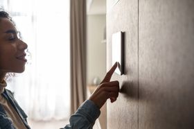 Woman touching a wall-mounted thermostat in a sunlit room