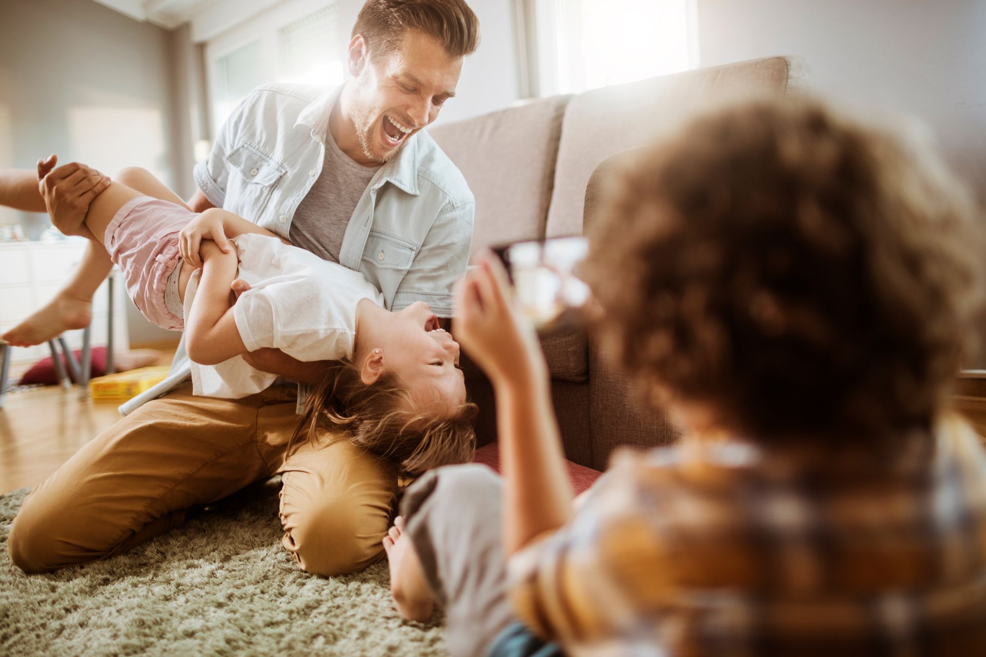 Adult playing with child on a living room floor while a toddler sits nearby