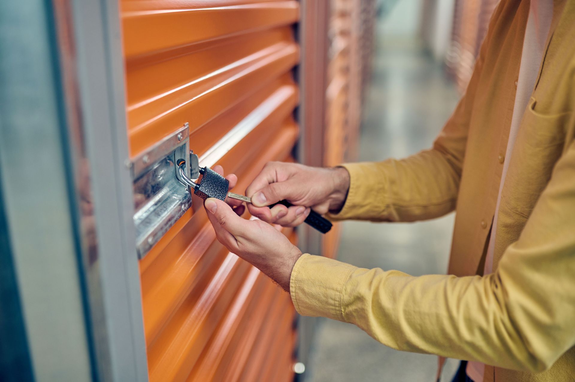 A worker unlocks a padlock placed on the orange door of a storage unit. A worker unlocks a padlock placed on the orange door of a storage unit.