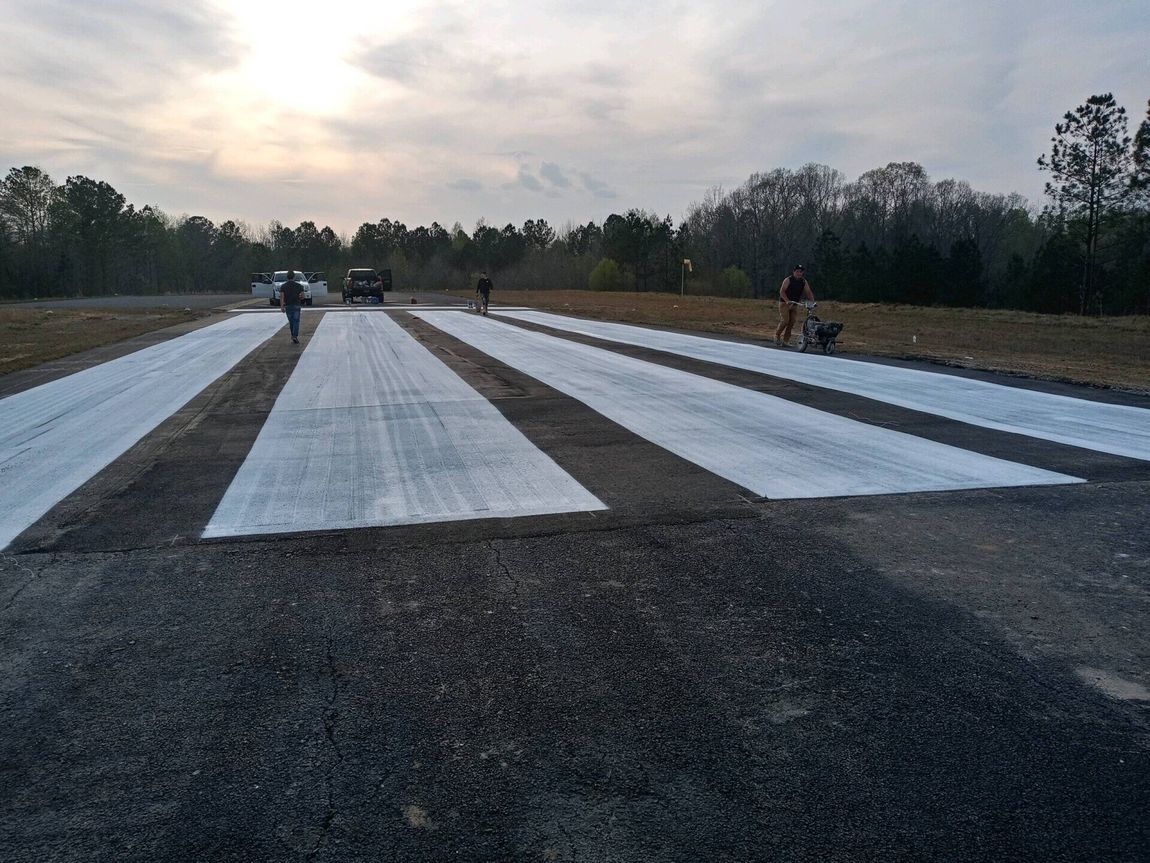 Asphalt and white concrete strips being worked on by three people at an outdoor construction site.