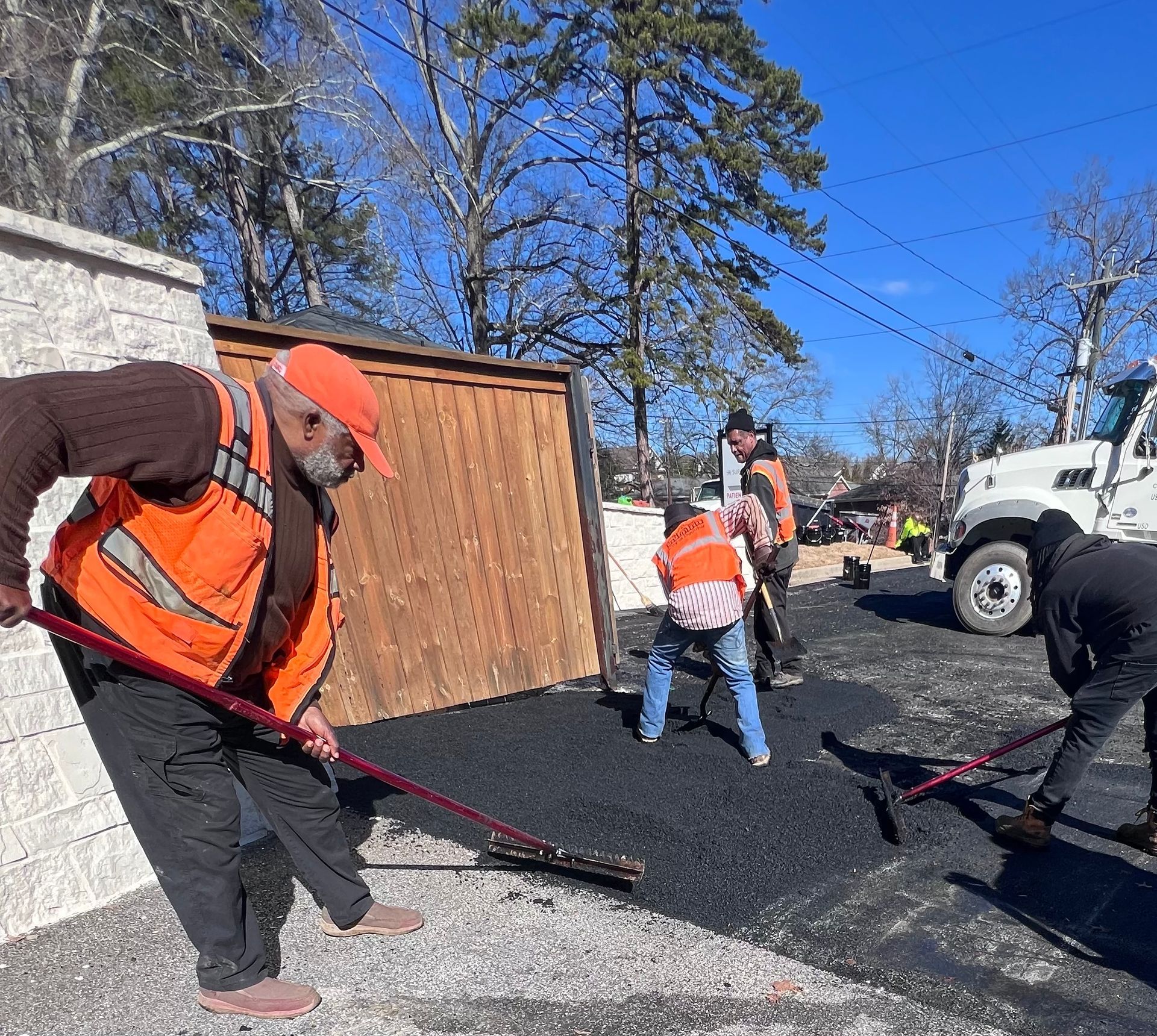 Asphalt paving in progress on a road, with two paving machines and a dump truck.