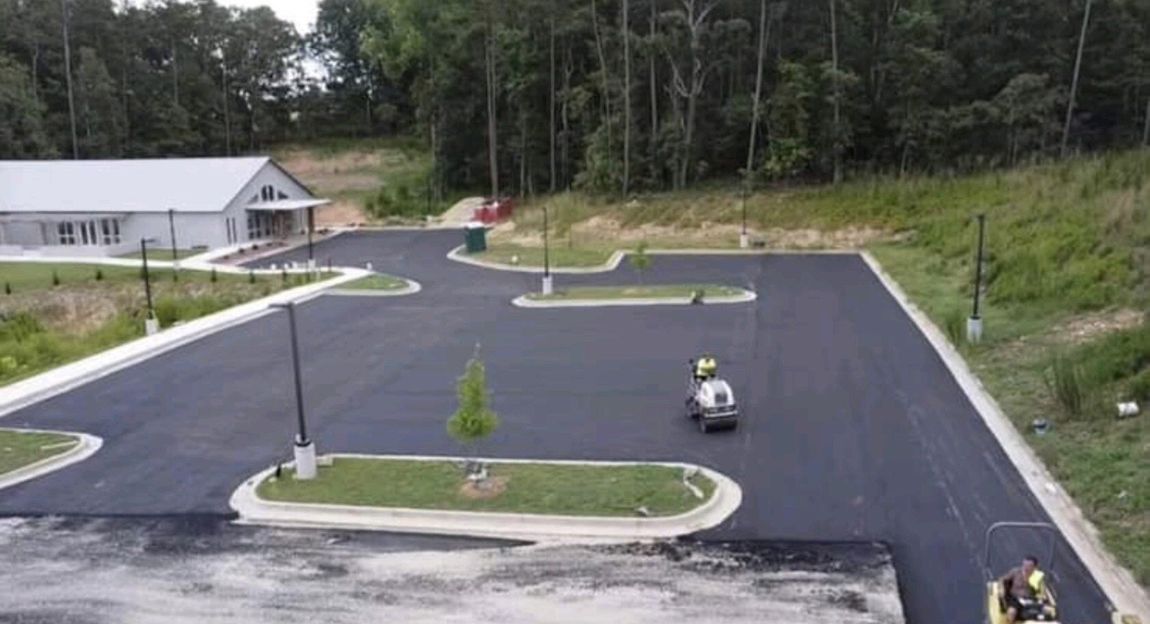 Newly paved parking lot with a building in the background and a worker operating equipment.