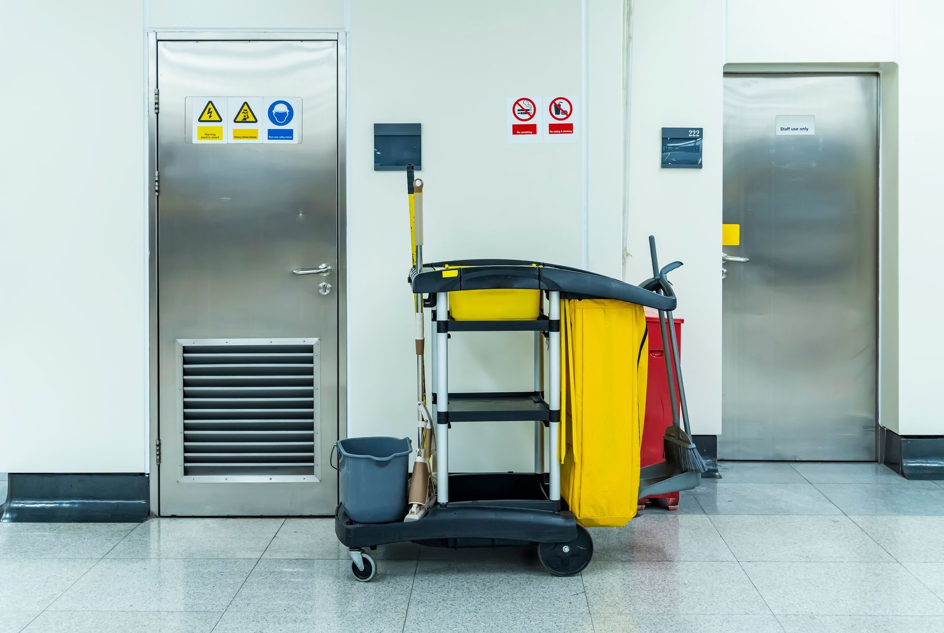 Airport hallway with metal doors, a cleaning cart, and warning signs on the wall