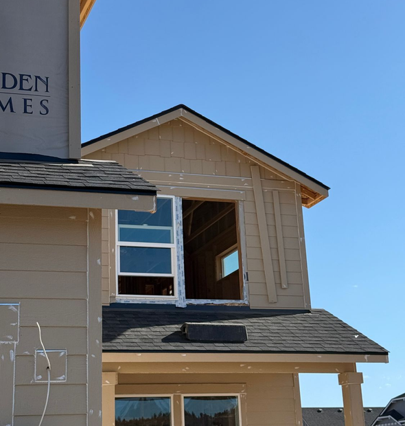 Partially built beige house with exposed window openings and dark gray shingles against a blue sky