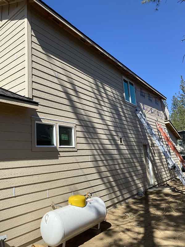 Side of beige house with a white propane tank and ladder beside a blue sky.