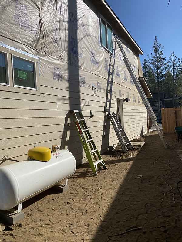 House exterior with ladders and utility tank beside a dirt foundation trench
