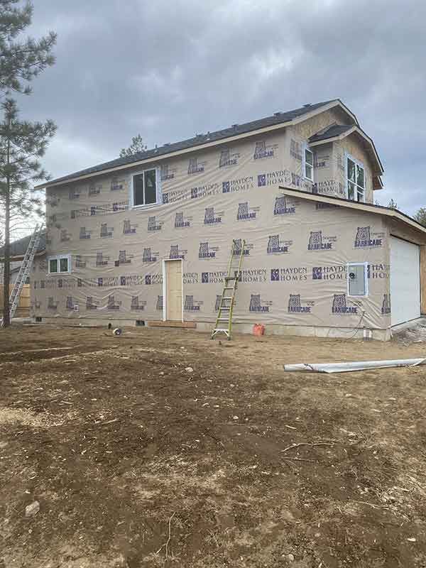 Two-story house under construction with wrapped exterior and bare dirt yard