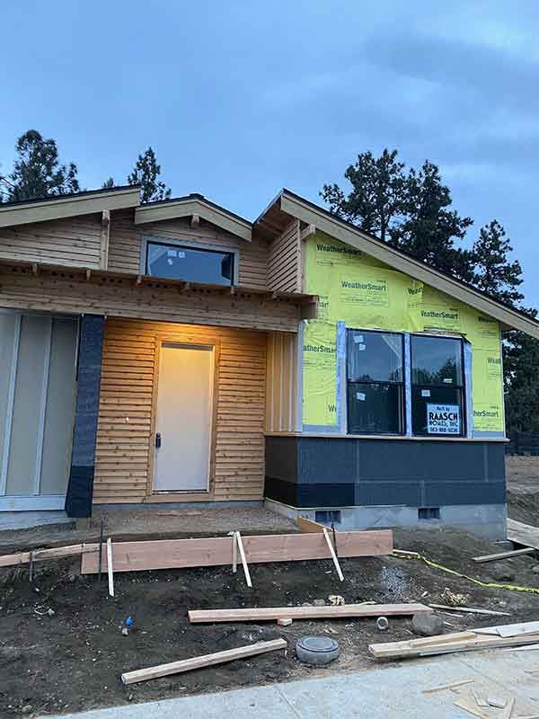Front of house under construction with exposed framing, yellow siding, and a lit front door at dusk