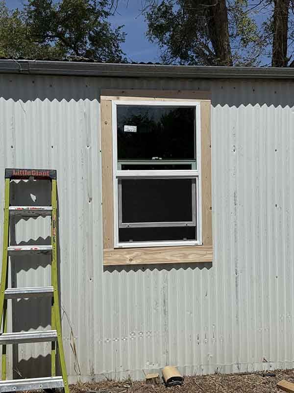 Corrugated metal wall with a window, wooden trim, and a ladder leaning on the left.