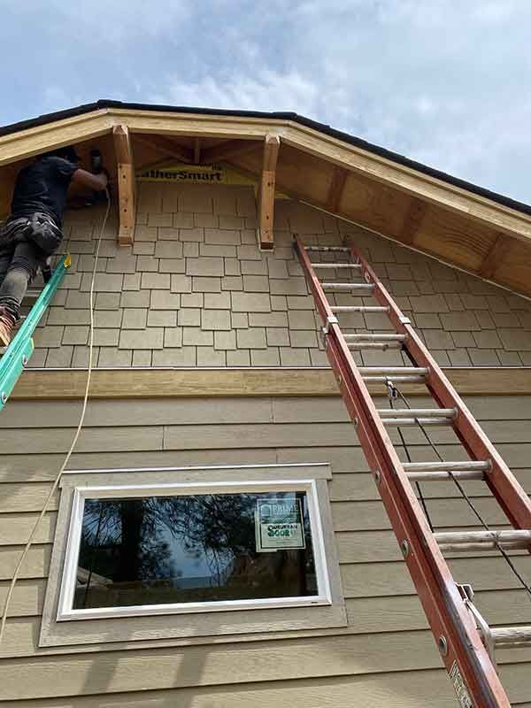 Person on ladder repairing roof on a beige house with another ladder against the wall
