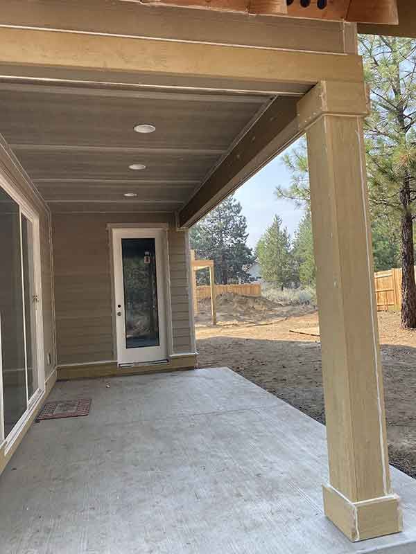 Covered front porch with beige columns, concrete floor, and a glass door overlooking a dry yard.