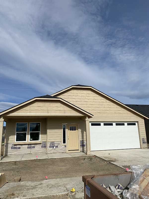 New beige single-story house under construction with a white garage door and blue sky above