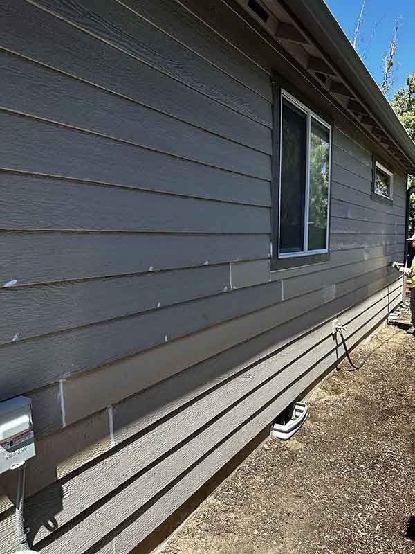 Exterior of a gray house with horizontal siding and a window along a dirt side yard.