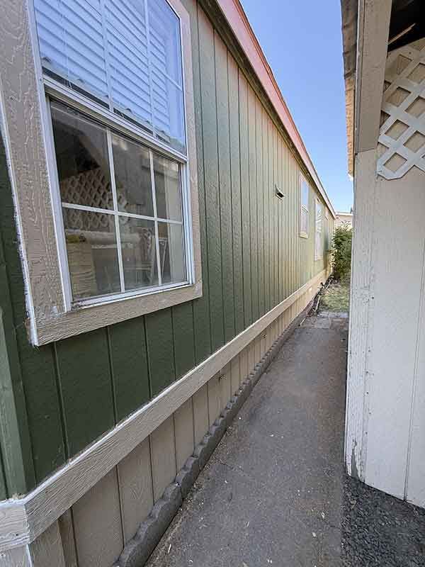 Narrow side yard between green and white buildings with a window and concrete walkway