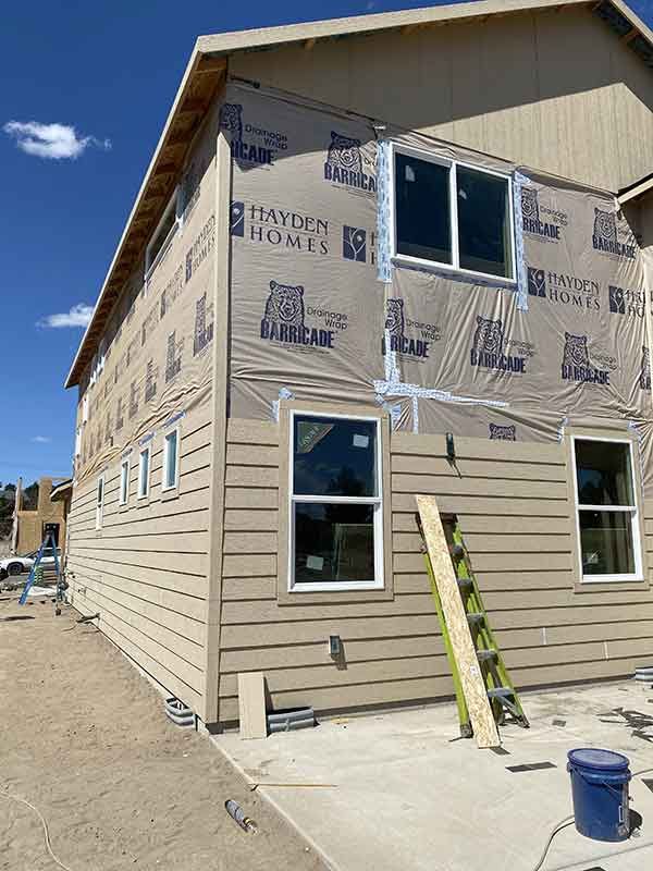 Partially clad tan house under construction with ladder, windows, and roof overhang on a sunny day