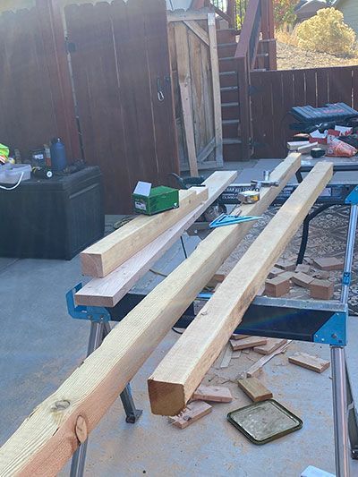 Wooden beams laid across two sawhorses in an outdoor workshop area