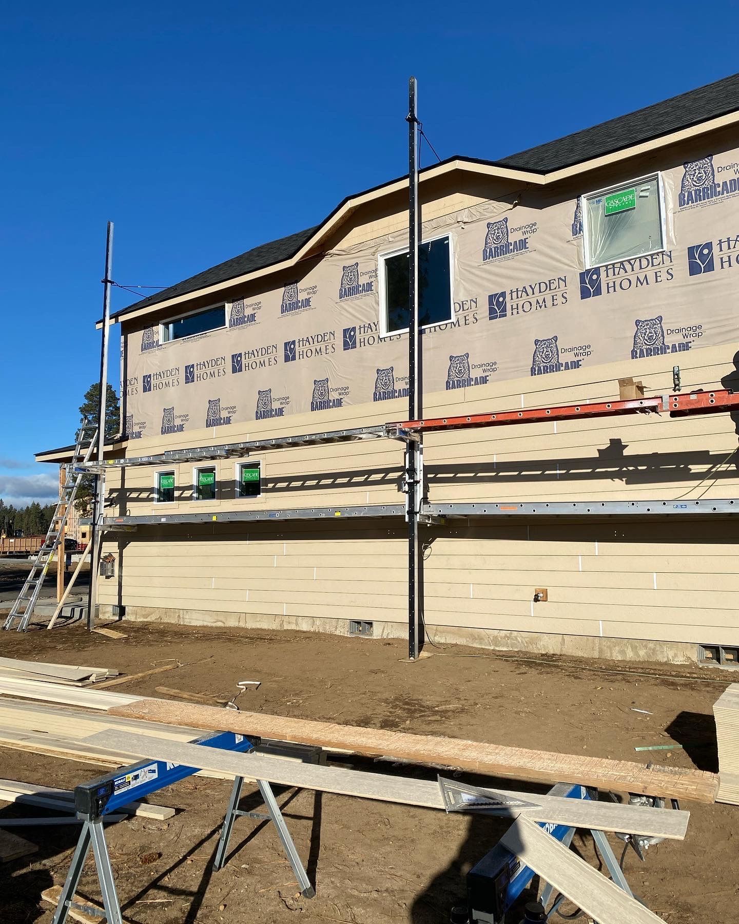 Partially built house exterior with scaffolding, exposed siding, and construction materials under a blue sky