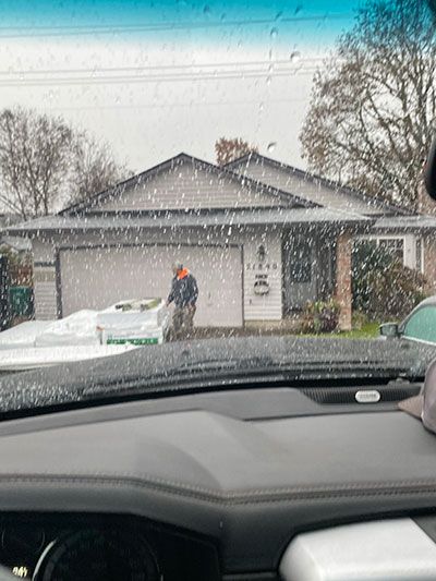 Snowy suburban house viewed through a car windshield, with a person near the front door and an open garage.