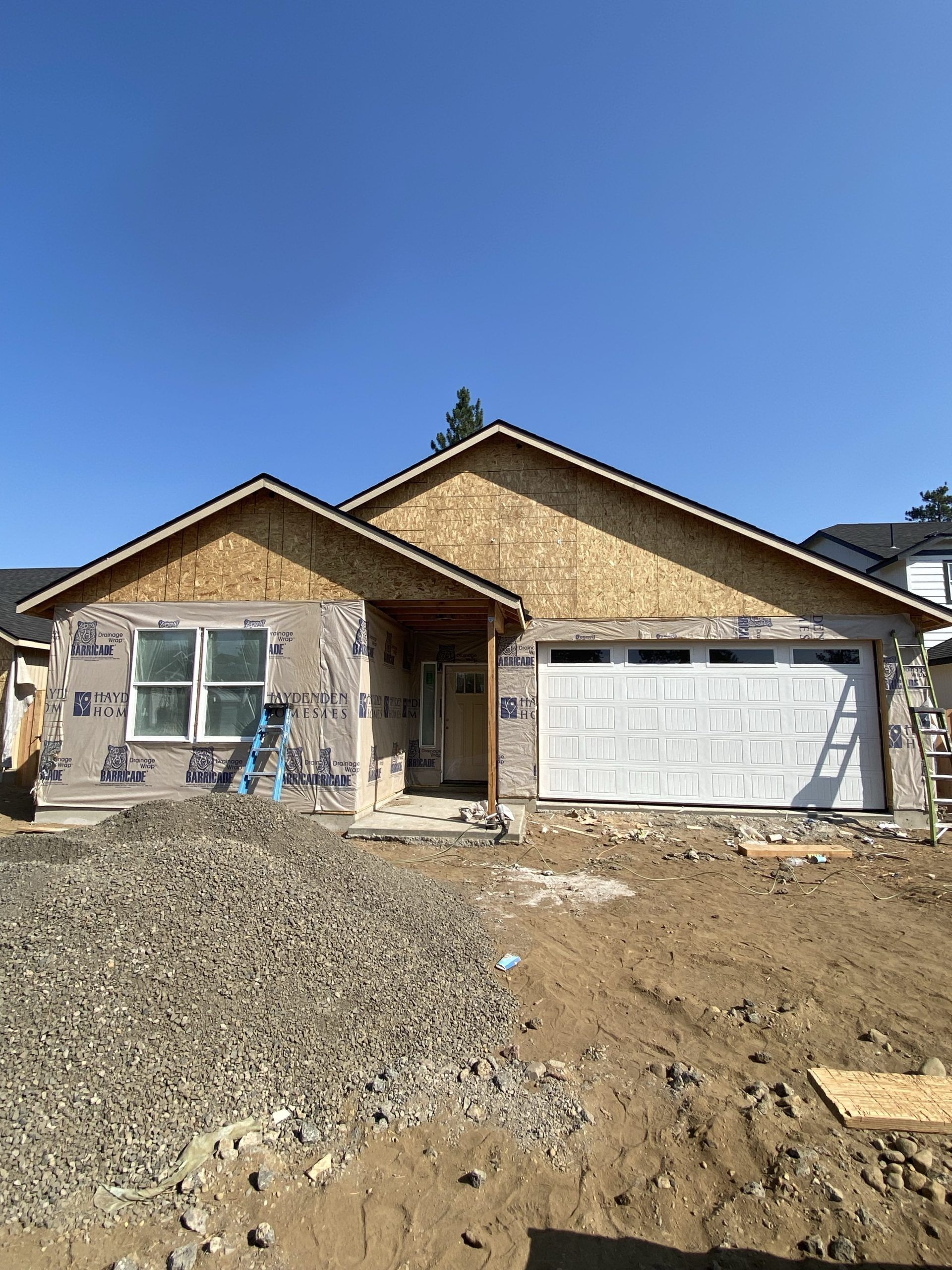 Single-story house under construction with gravel foreground and blue sky