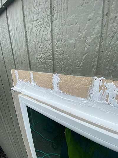 Caulked trim above a white window frame on a green exterior wall