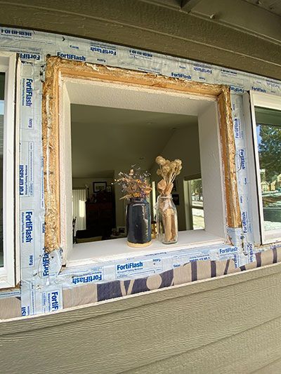 Unfinished window opening with masking tape, overlooking a room with vases on the sill.