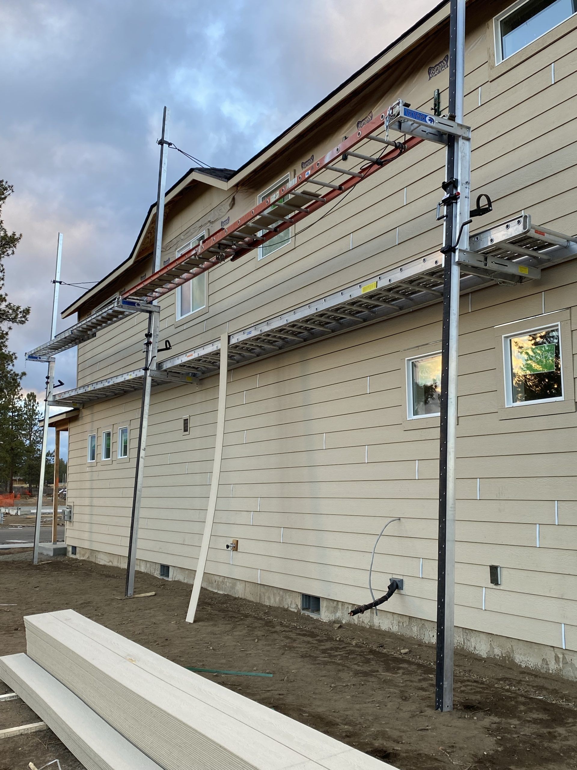 House exterior under renovation with scaffolding and stacked white siding boards in the foreground