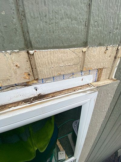Damaged exterior wall above a window, with peeling siding and exposed wood trim
