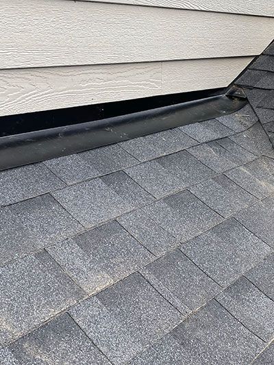 Loose roof shingles beneath damaged siding on a house exterior