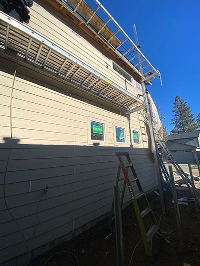 House exterior under renovation with scaffolding, ladders, and beige siding under a clear blue sky