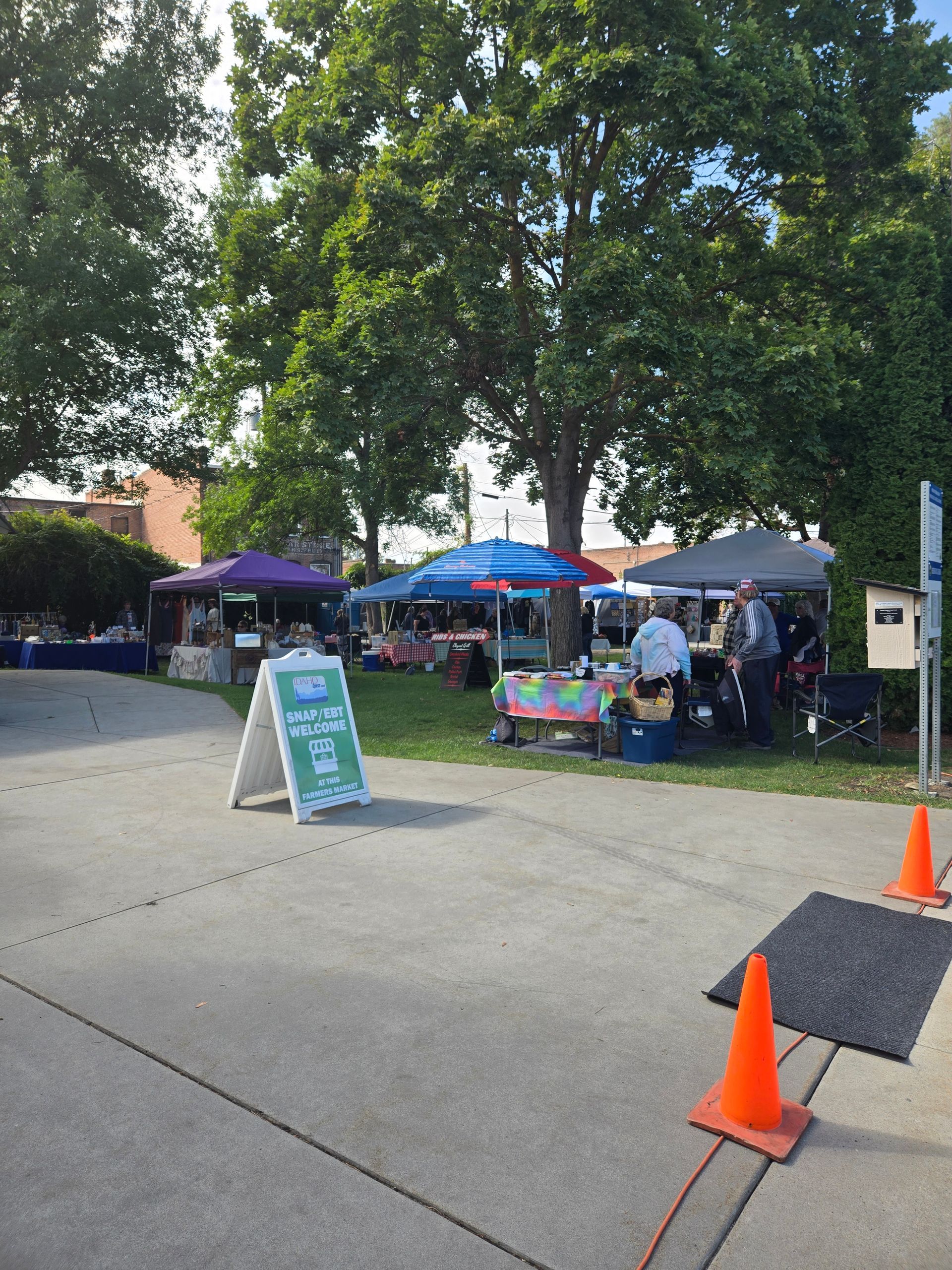 Outdoor farmers market with tents, produce, and a sign on a sunny day.