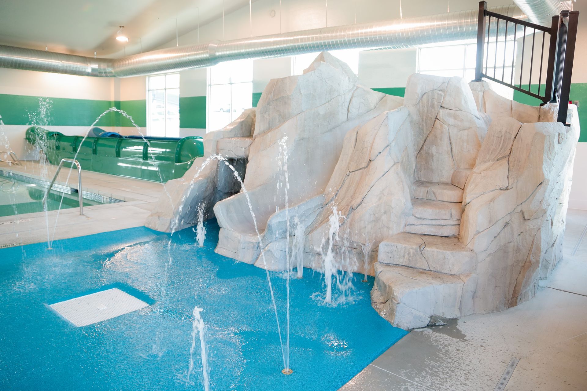 Indoor pool with water slides and fountain jets beside white rock-style seating area